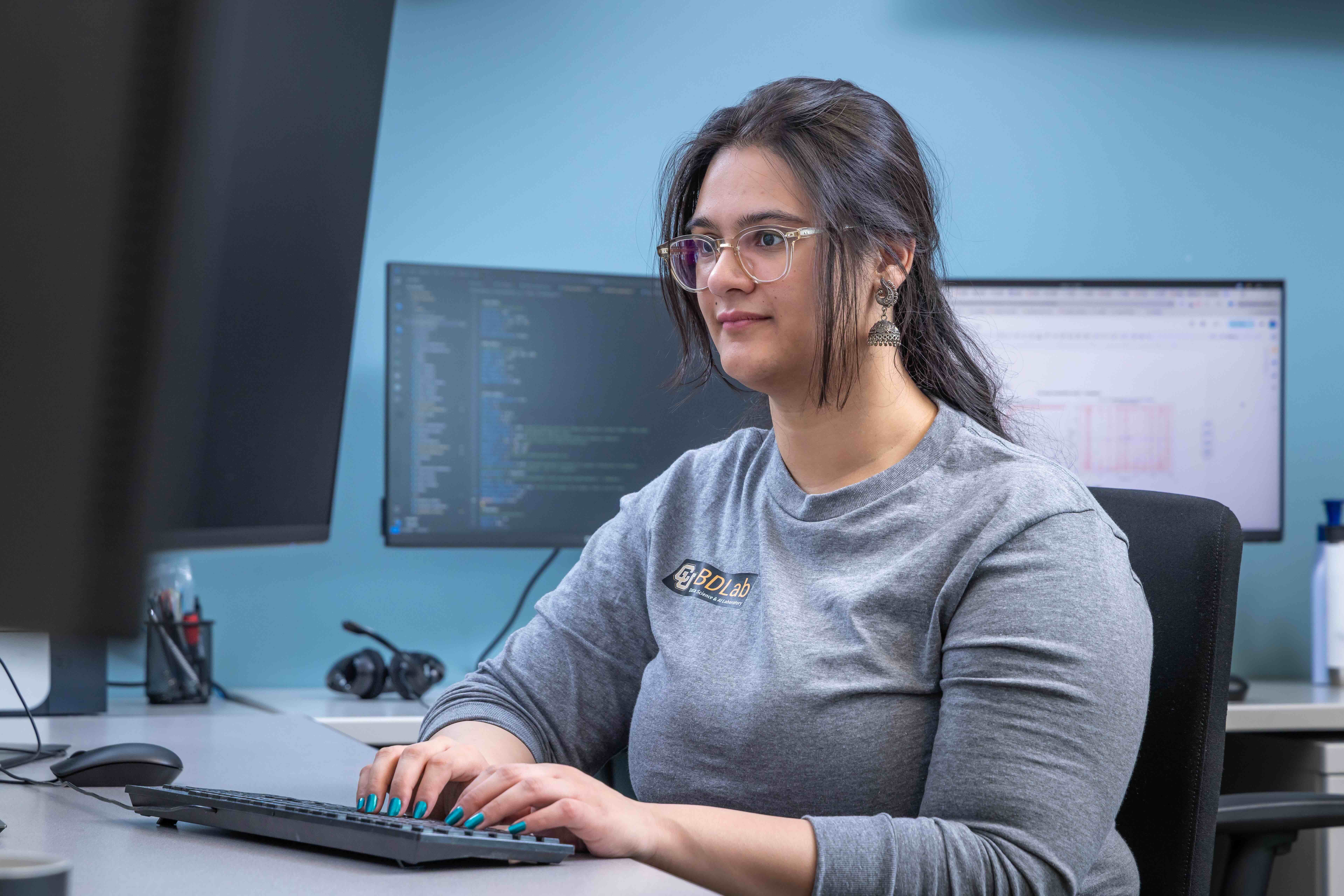 Woman sits at computer hile surrounded by computers